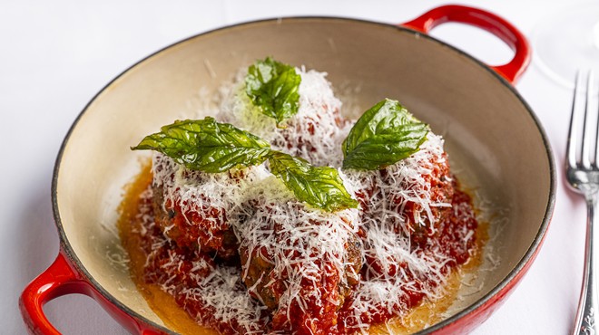 Meatballs topped with basil and finely shredded cheese in a red enameled iron pot
