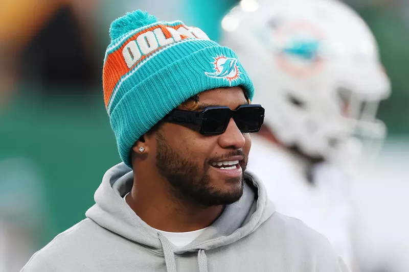 Image: Sporting sunglasses and a pom-pom-topped team-issue knit hat, Tua Tagovailoa #1 of the Miami Dolphins looks on before the game against the New York Jets at MetLife Stadium on January 05, 2025, in East Rutherford, New Jersey