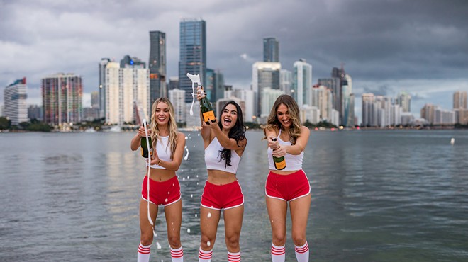 Three women in red shorts popping bottles of Champagne.