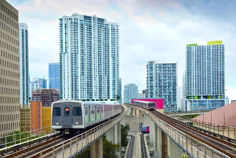 Image: Two metro trains on elevated platforms with the Miami skyline in the background