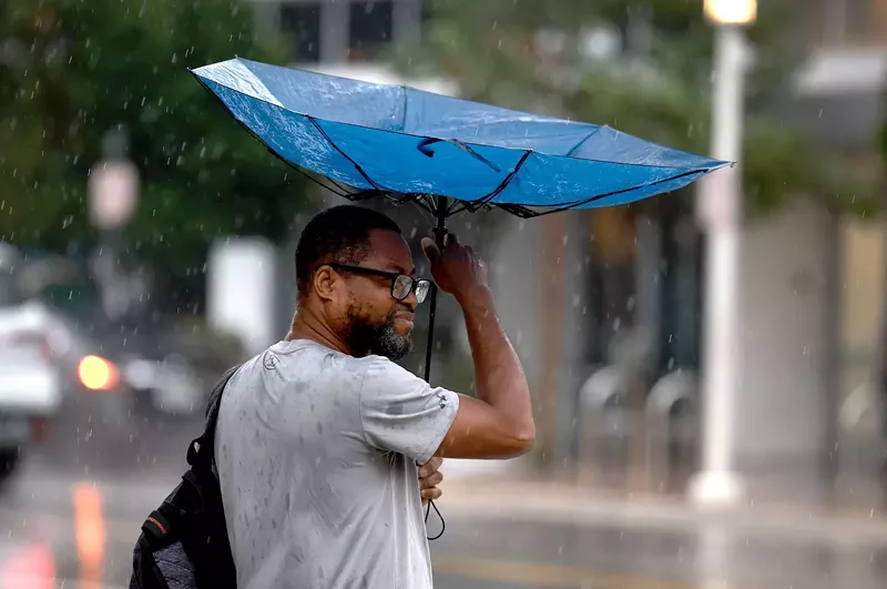 Image: Wind blows a pedestrian's umbrella inside out as rain inundates the area on November 15, 2023, in Miami Beach, Florida, leaving Miami-Dade County soaked and causing concern for potential flooding.
