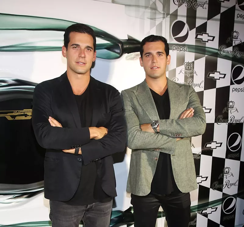 Image: Twin brothers Alon and Oren Alexander stand with arms crossed while posing for photo at an event