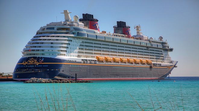 The Disney Dream cruise ship –– a massive vessel colored navy, white, and red –– arrives to shore in turquoise blue waters Castaway Cay, Bahamas.