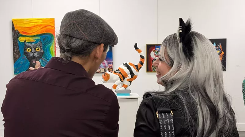 Image: two people look at a sculpture of a cat inside a gallery