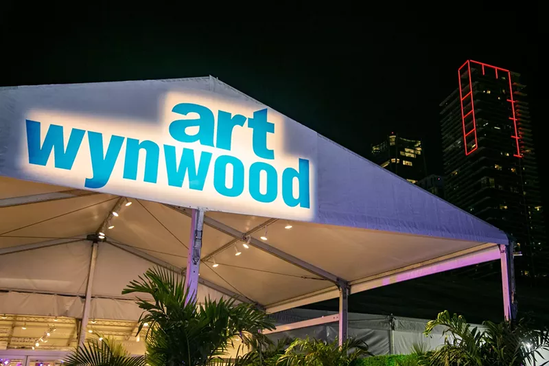 Image: The words "Art Wynwood" spotlighted on the tent with the downtown Miami skyline in the background