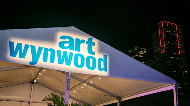 The words "Art Wynwood" spotlighted on the tent with the downtown Miami skyline in the background