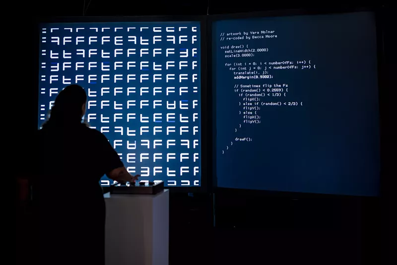 Image: A person stands in front of a large projection of code