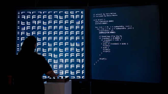 A person stands in front of a large projection of code
