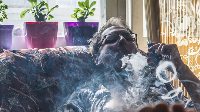 A man blows smoke rings from a hookah on his couch