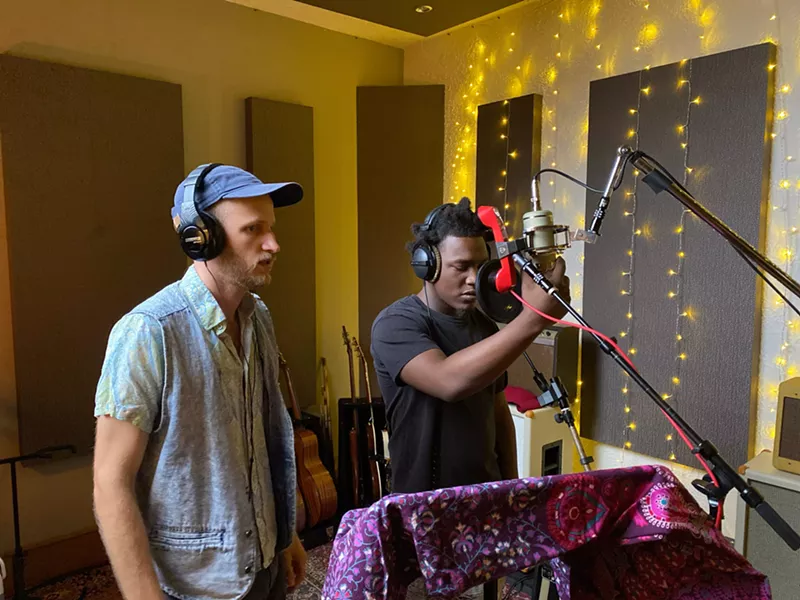 Image: two men, one white, the other Black, wearing headphones in a modest recording studio