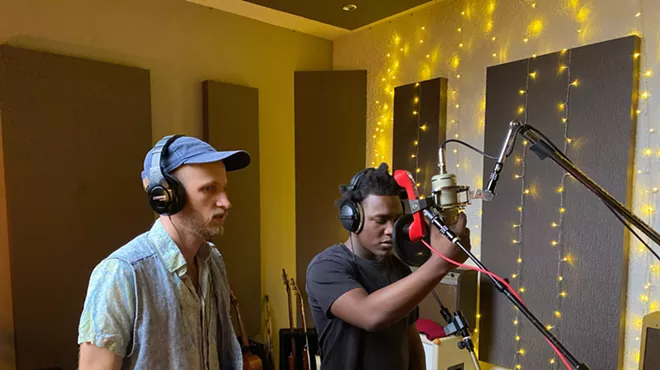 two men, one white, the other Black, wearing headphones in a modest recording studio
