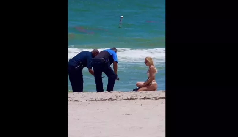 Image: A woman in a bikini and two police officers crouch over a brick of white powder on the beach