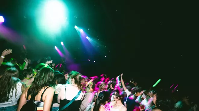 A group of young people dancing in a club. under green and fuchsia lights.