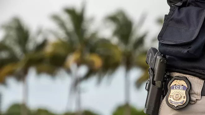 An immigration officer with an ICE badge next to palm trees.