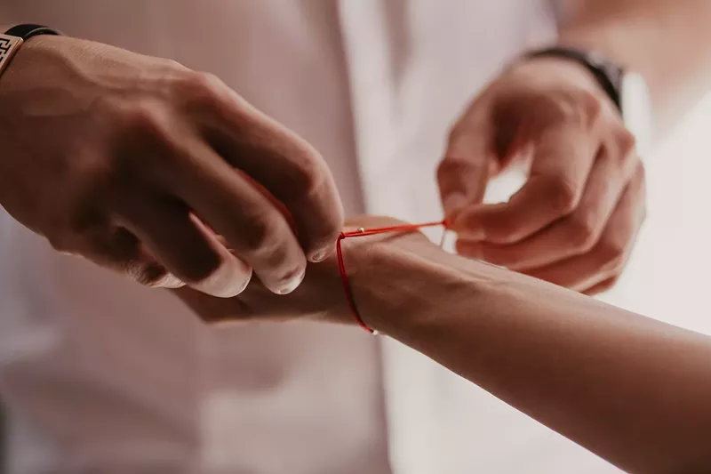 Image: A man ties a red string bracelet on a woman's hand