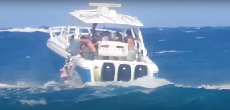 Image: A boat full of teenagers navigates rough waters as one boy dumps a trash can full of garbage into the ocean