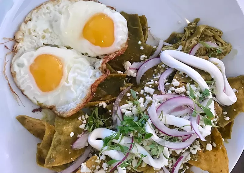 Image: Chilaquiles: Tortilla chips, shredded chicken, sunny-side up eggs, queso fresco, sour cream, ranchero sauce, and poblano sauce.