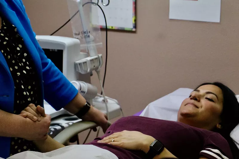 Image: A woman holds a doctor's hand as she lies on an examining room table.