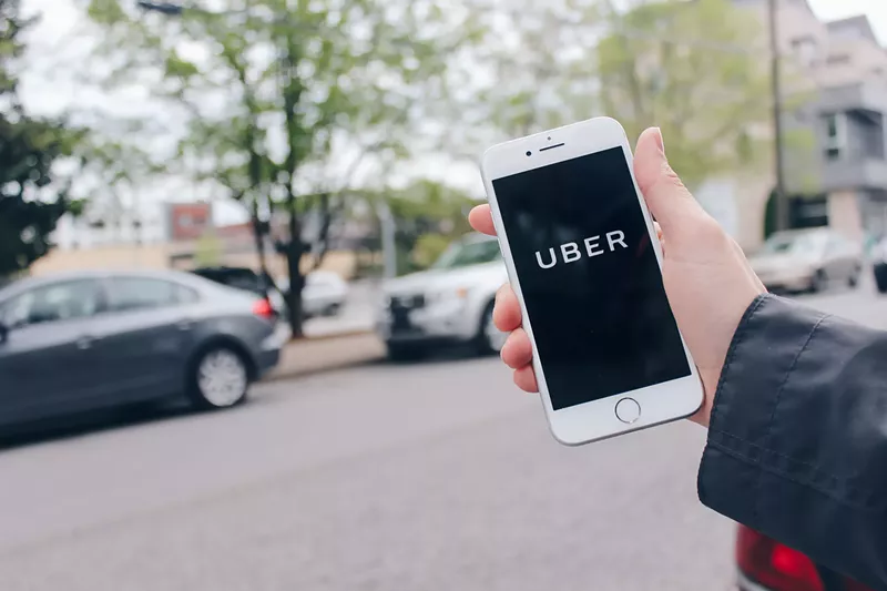 Image: a hand holds up a phone with the Uber app on the screen