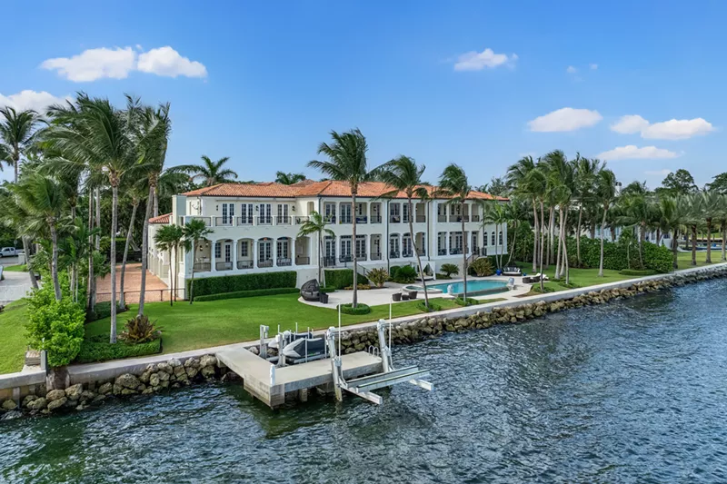 Image: Backyard view of large cream waterfront mansion
