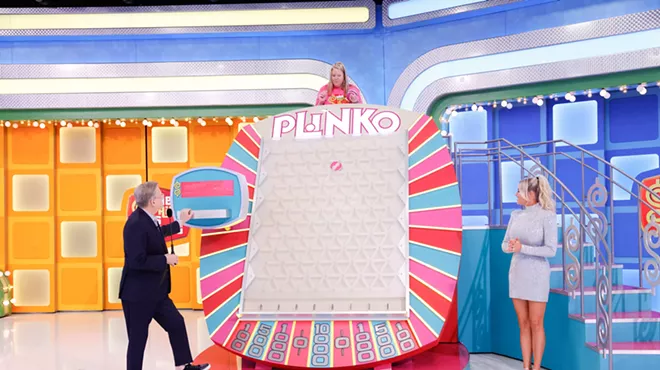 A game show host and model stand on either side of a gameboard reading "Plinko." A woman stands above the gameboard