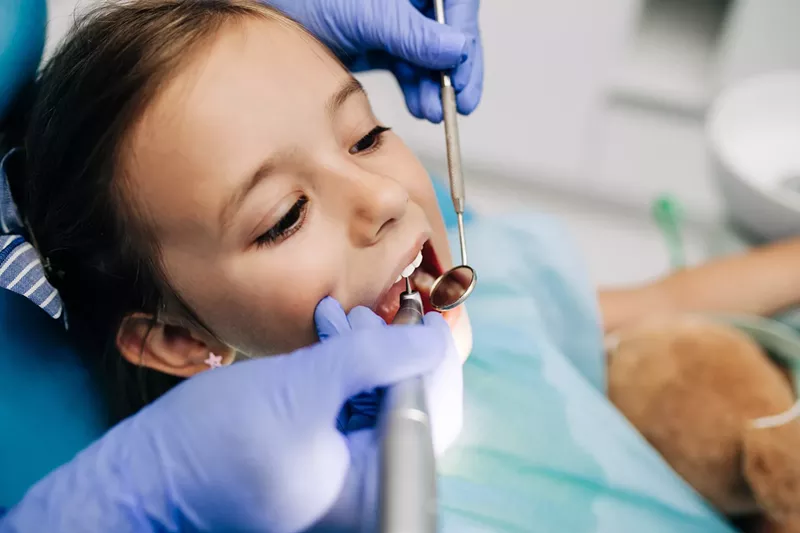 Image: Cute little girl sitting in a dental chair and receiving dental treatment.