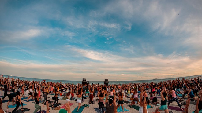 A large group of people doing yoga on the beach at dawn