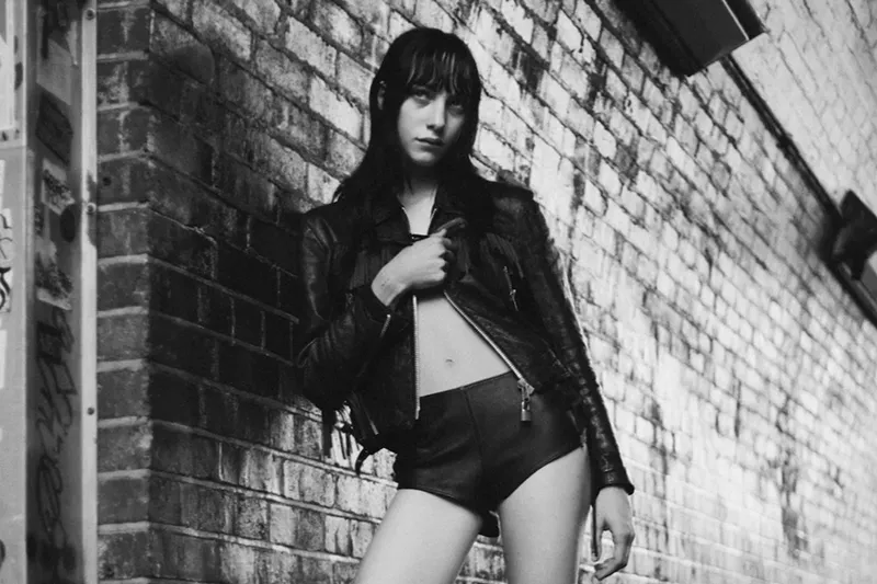 Image: Black and white photo of Devon Ross leaning on a brick wall