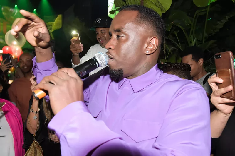 Image: Closeup of rapper Sean "Diddy" Combs holding a microphone to his lips, surrounded by a crowd holding out their phone cameras