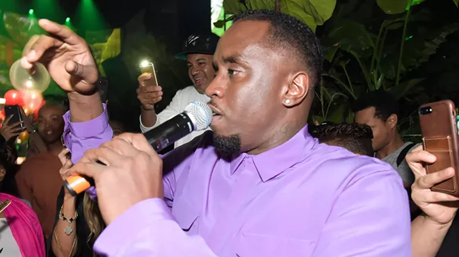 Closeup of rapper Sean "Diddy" Combs holding a microphone to his lips, surrounded by a crowd holding out their phone cameras