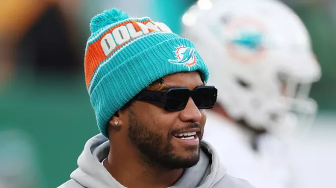 Sporting sunglasses and a pom-pom-topped team-issue knit hat, Tua Tagovailoa #1 of the Miami Dolphins looks on before the game against the New York Jets at MetLife Stadium on January 05, 2025, in East Rutherford, New Jersey