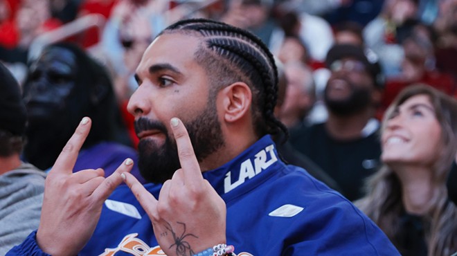 Closeup of rapper Drake throwing up hand signs at a Houston Rockets game.