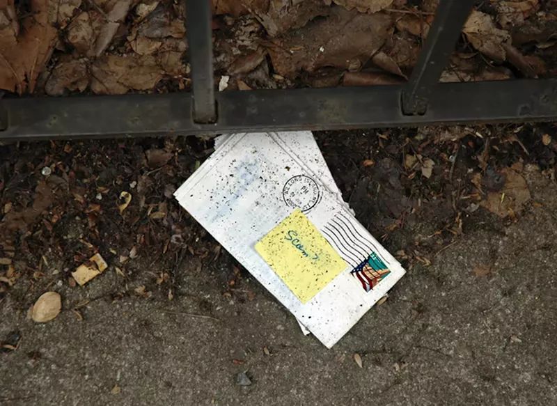 Image: An envelope on the floor with a sticky note on top that reads "Scam?"