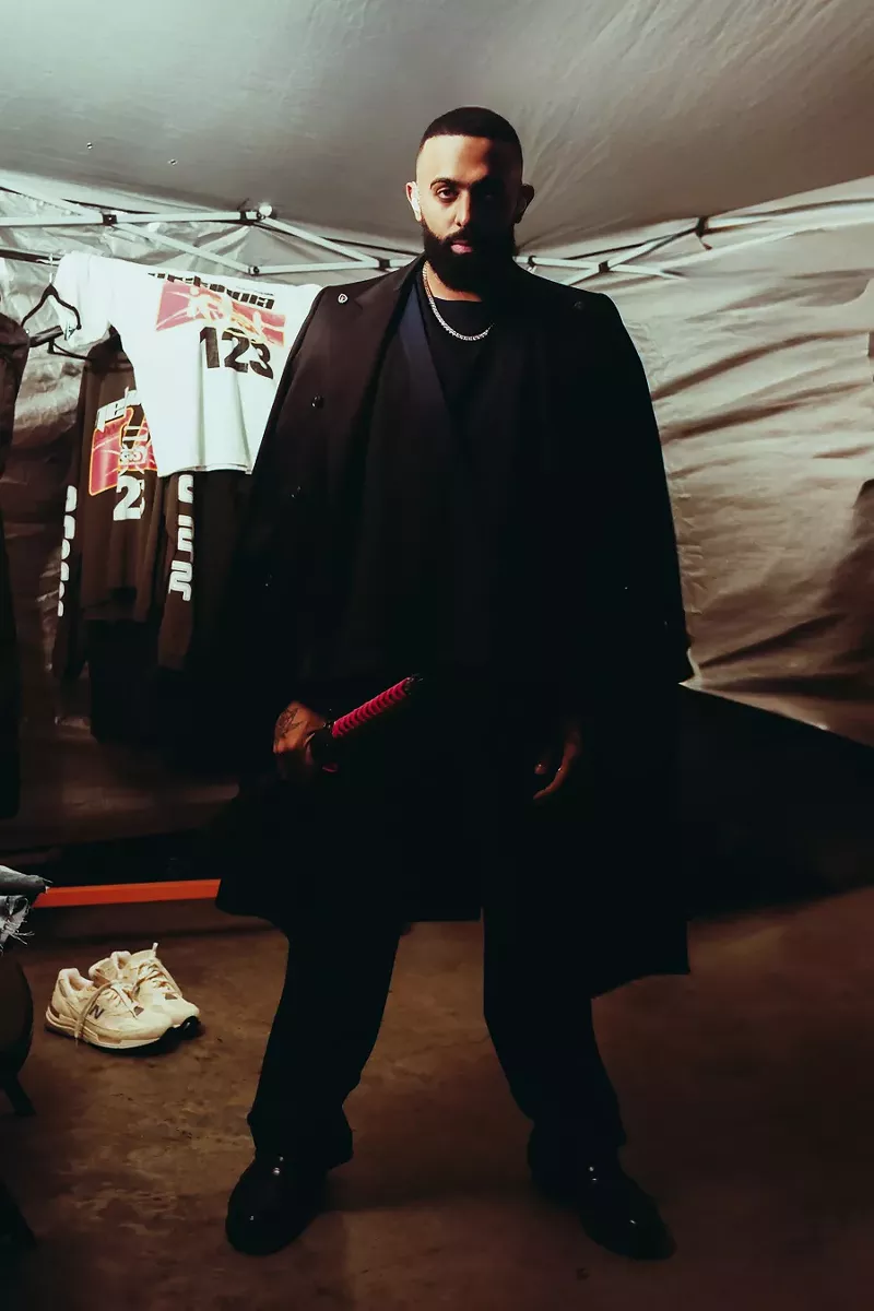 Image: Picture of a man looking at the camera, wearing black, and holding a katana.