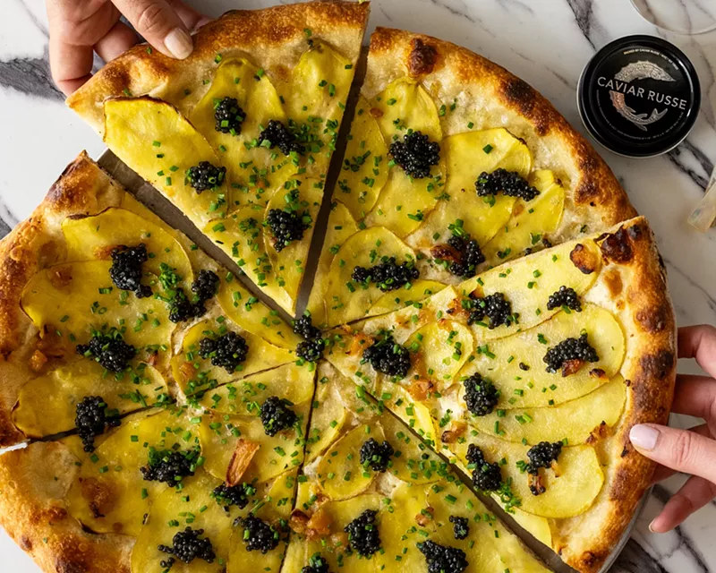 Image: White pizza topped with caviar and a hand pulling it