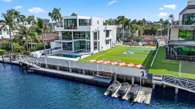Waterfront white mansion with Miami Dolphins football field next to it