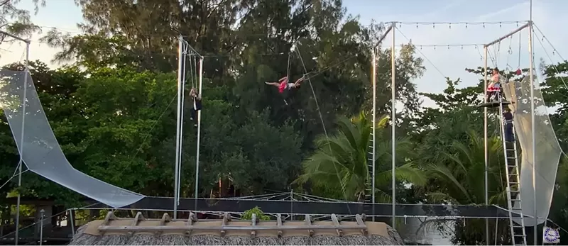 Image: A trapeze artist swings in the air in a modular trapeze rig set up in a Miami man's backyard