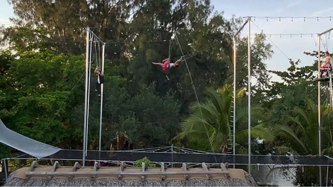 A trapeze artist swings in the air in a modular trapeze rig set up in a Miami man's backyard