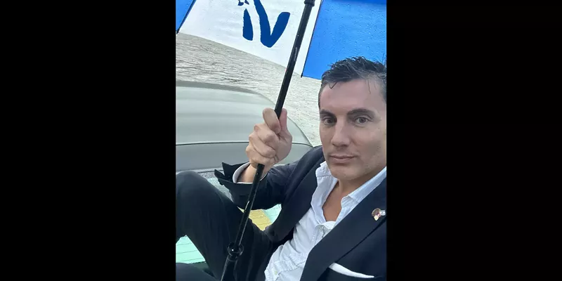 Image: Fabián Basabe sitting on top of his car in a flood, with an umbrella