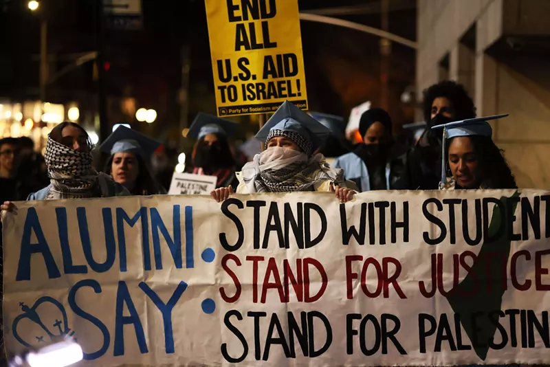Image: Protesters hold a large white sign, declaring, "Stand with students, stand for justice, stand for Palestine."