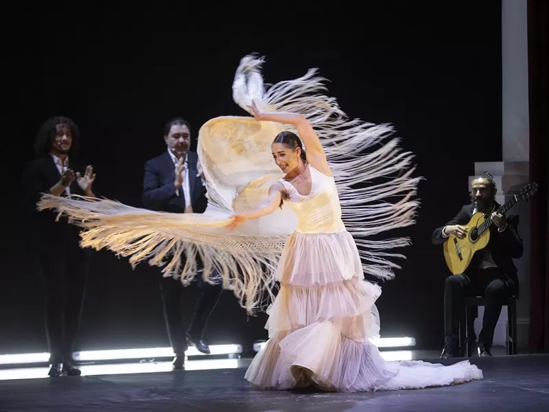 Image: Flamenco dancer on stage in a white costume as the fringe moves in the air
