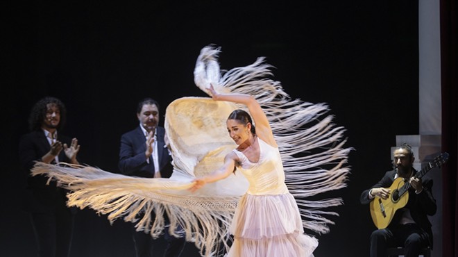 Flamenco dancer on stage in a white costume as the fringe moves in the air