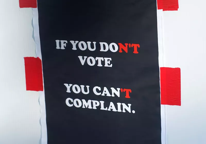 Image: photo of a red, white, and blue sign that says "If you don't vote, you can't complain" but owing to its coloration can be read to say "if you do vote, you can complain"