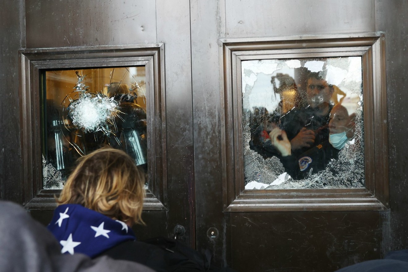 A Capitol police officer looks out of a broken window at the U.S. Capitol.