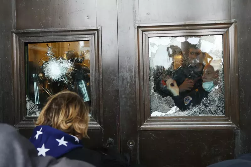 Image: A Capitol police officer looks out of a broken window at the U.S. Capitol.