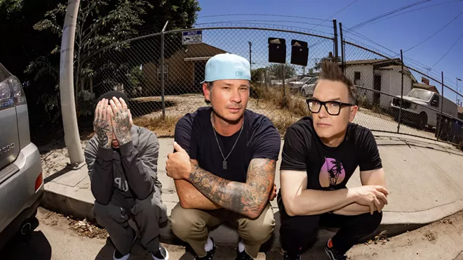 Photo of Blink-182 sitting on a curb.