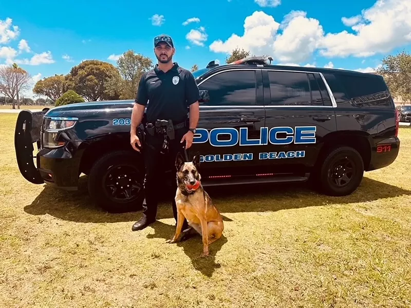 Image: uniformed police officer standing with his K-9 in front of a black police cruiser