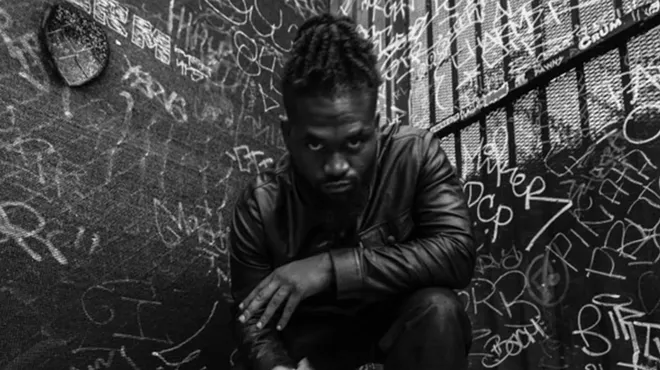 black and white picture of a young man by a graffiti-covered wall.