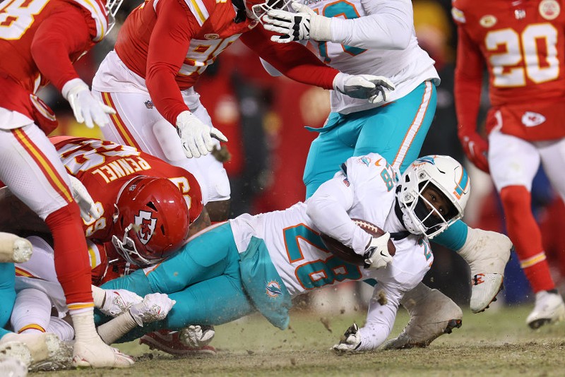 De'Von Achane of the Miami Dolphins is tackled by Kansas City Chiefs defensive lineman Mike Pennel during the AFC Wild Card playoffs at frigid Arrowhead Stadium on January 13, 2024.