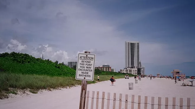 a sign on the sands on the beach reads "Attention: Beyond this point you may encounter nude bathers"